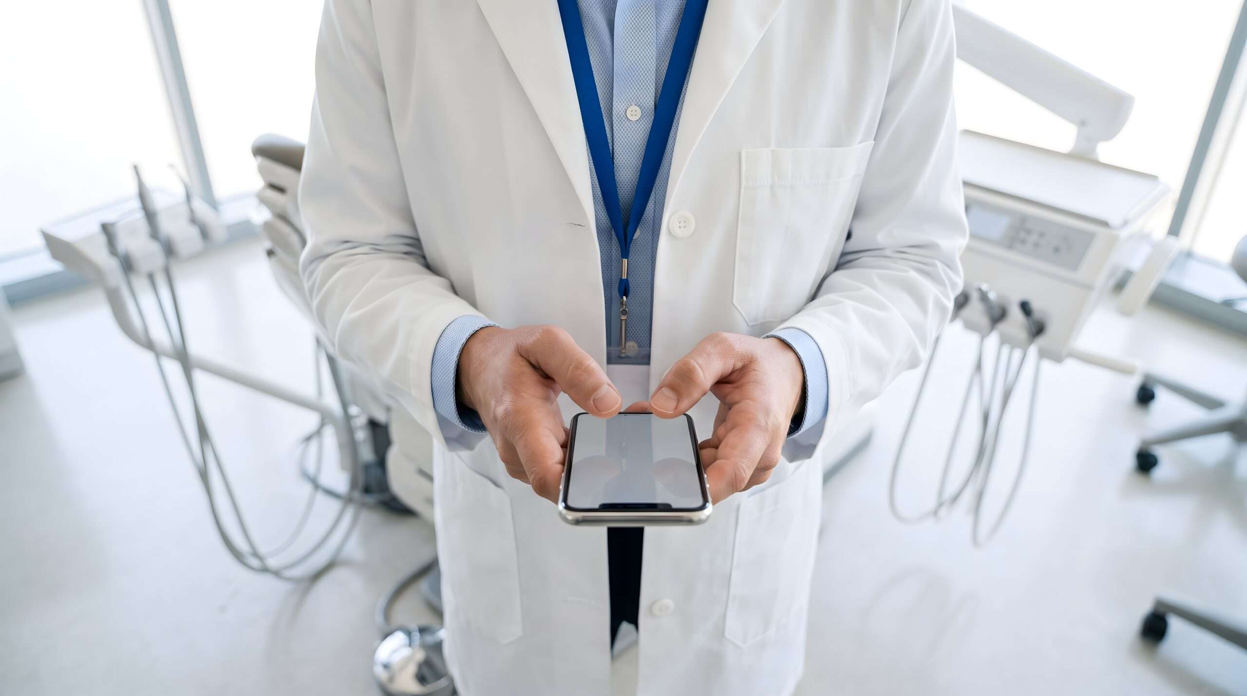 Doctor in white lab coat using smartphone for digital health records while standing in modern dental operatory. Modern Technology